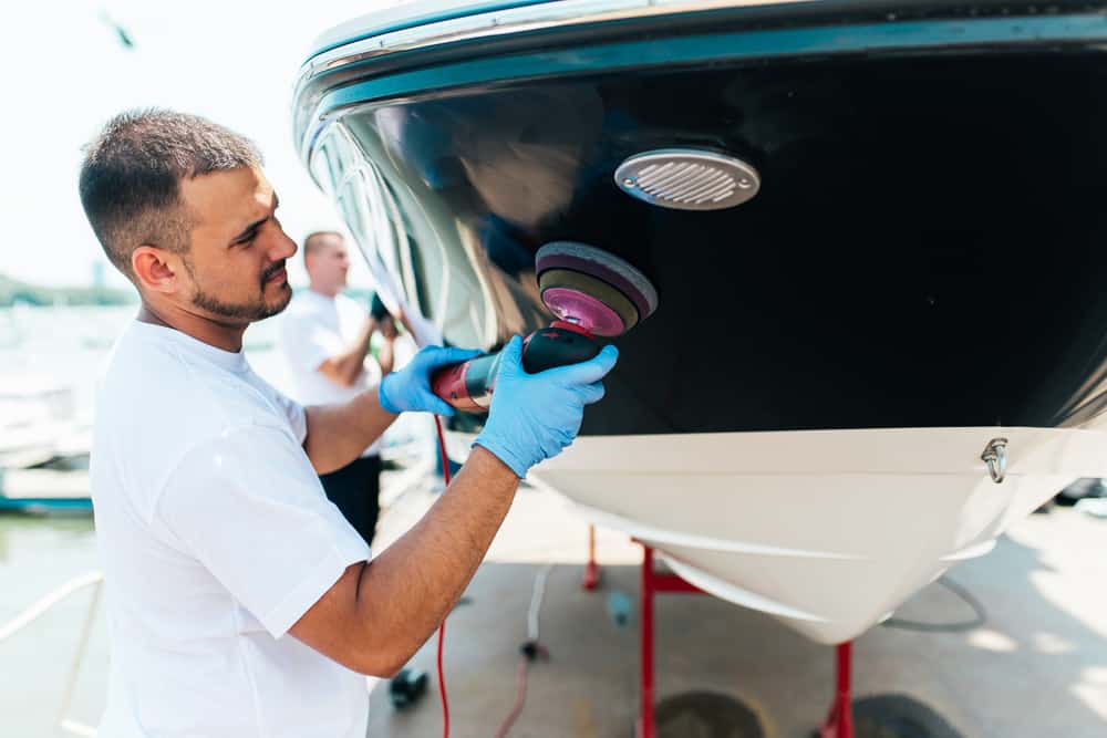 Man with orbital polisher polishing boat in marina